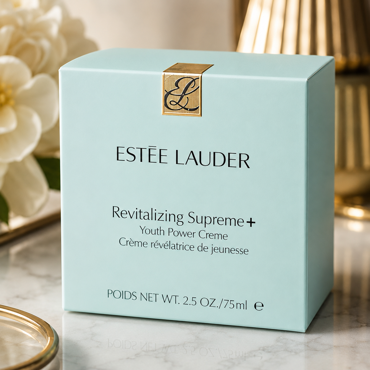 Estée Lauder Revitalizing Supreme+ Youth Power Creme packaging on a marble surface with flowers in the background